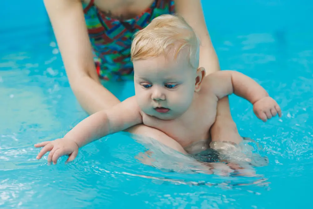 A 6-month-old baby learns to swim with a coach in the pool. Swimming pool for babies. Children's development